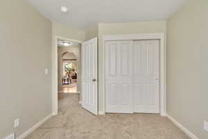 Unfurnished bedroom featuring arched walkways, light carpet, and a closet