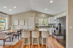 Kitchen with black refrigerator with ice dispenser, electric stove, white cabinets, backsplash, and a kitchen island