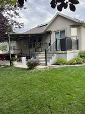 Rear view of property with solar panels, a patio area, stucco siding, and a lawn