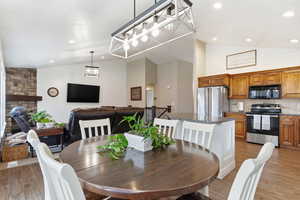 Dining area with lofted ceiling, light wood-style flooring, recessed lighting, wooden walls, and a stone fireplace