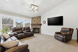 Living room with a stone fireplace, carpet floors, and lofted ceiling