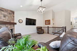 Living room with lofted ceiling, carpet flooring, a fireplace, and suspended lighting