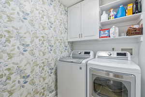 Laundry area with wallpapered walls, cabinet space, and independent washer and dryer