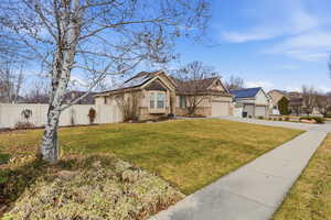 View of front of home featuring driveway, stucco siding, solar panels, an attached garage, and a gate