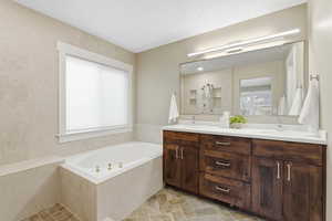Full bathroom featuring a bath, double vanity, and stone finish floors