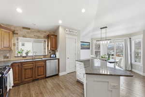 Kitchen featuring dark stone countertops, a kitchen island, backsplash, light wood-type flooring, and stainless steel appliances