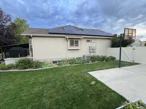 View of property exterior with roof mounted solar panels, a gate, stucco siding, and roof with shingles