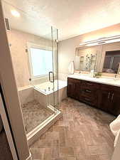 Full bathroom with a garden tub, double vanity, a textured ceiling, and a stall shower