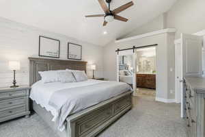 Bedroom featuring a barn door, vaulted ceiling, light carpet, a ceiling fan, and ensuite bathroom