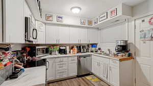 Kitchen with stainless steel appliances, white cabinetry, backsplash, and light wood-style floors