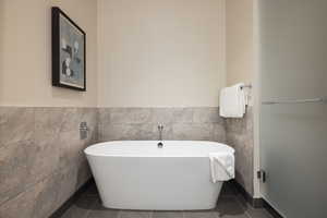 Full bath with a freestanding bath, tile walls, and dark tile patterned floors