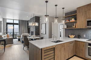 Kitchen with modern cabinets, wood finish cabinetry, floor to ceiling windows, stainless steel appliances, and decorative light fixtures