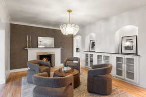 Living area featuring light wood-style floors, ornamental molding, a tiled fireplace, a chandelier, and arched walkways