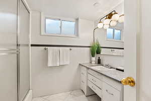 Bathroom with vanity, an enclosed shower, wainscoting, tile walls, and healthy amount of natural light