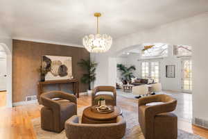 Sitting room featuring arched walkways, french doors, light wood-style floors, crown molding, and hanging lights