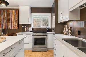 Kitchen with stainless steel gas range oven, white cabinetry, light stone countertops, and modern cabinets