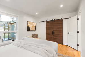 Bedroom with a barn door, light wood-type flooring, and recessed lighting