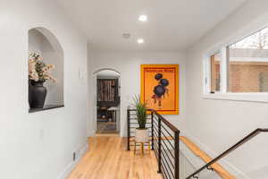 Hallway featuring arched walkways, light wood-style floors, an upstairs landing, and recessed lighting