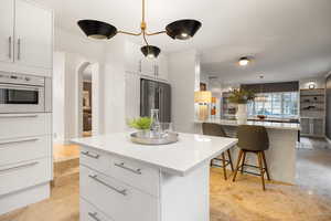 Kitchen featuring white cabinetry, decorative light fixtures, a kitchen breakfast bar, arched walkways, and high end fridge