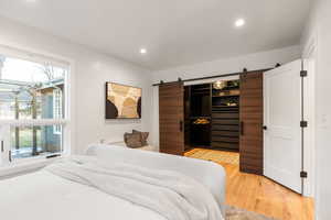 Bedroom featuring a barn door, light wood-style flooring, a spacious closet, and recessed lighting