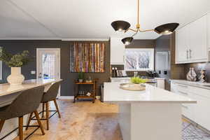 Kitchen with white cabinetry, a breakfast bar area, plenty of natural light, a kitchen island, and ornamental molding