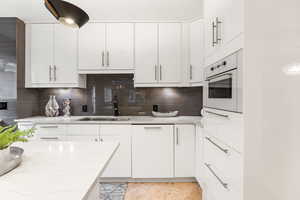 Kitchen featuring white cabinets, oven, modern cabinets, light stone counters, and tasteful backsplash