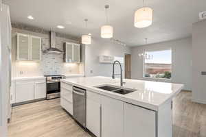 Kitchen featuring glass fronted cabinets, tasteful backsplash, a center island with sink, white cabinets, and light wood-type flooring