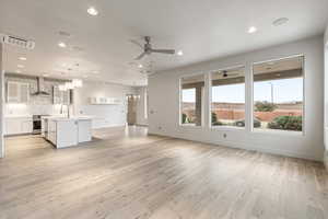 Unfurnished living room featuring light wood-type flooring, ceiling fan, and hanging lights