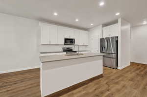 Kitchen with stainless steel appliances, white cabinets, quartz countertops, light wood finished floors, an island with sink, and recessed lighting
