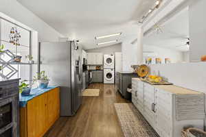 Two tone kitchen with two tone color scheme, stainless steel fridge, stacked washer and clothes dryer, dark wood-style flooring, and lofted ceiling with beams