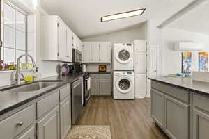 Laundry area featuring healthy amount of natural light, dark wood-type flooring, stacked washer and clothes dryer, and lofted ceiling