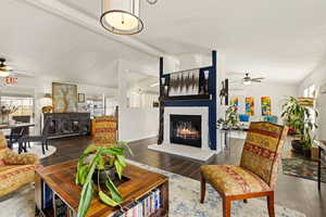 Living area with ceiling fan, beamed ceiling, wood finished floors, and a glass covered fireplace