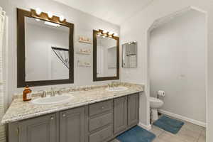 Bathroom with double vanity, light tile patterned flooring, and a textured wall