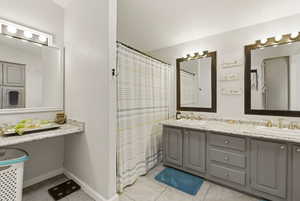 Full bathroom with double vanity, curtained shower, and light tile patterned flooring
