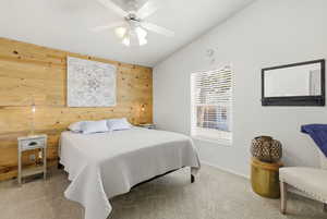 Bedroom featuring wooden walls, light colored carpet, vaulted ceiling, and a ceiling fan