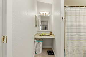 Full bathroom featuring a textured wall, a shower with shower curtain, vanity, and light tile patterned flooring