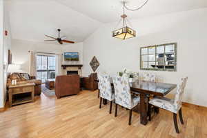 Dining space featuring vaulted ceiling, a ceiling fan, a fireplace, and light wood finished floors