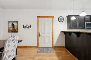 Kitchen with light wood-type flooring, a kitchen breakfast bar, stainless steel microwave, decorative light fixtures, and dark cabinetry