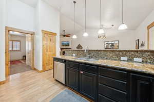 Kitchen featuring dark cabinetry, light stone countertops, light wood finished floors, decorative light fixtures, and vaulted ceiling