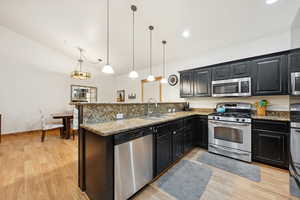 Kitchen featuring dark cabinetry, dark stone countertops, stainless steel appliances, a peninsula, and pendant lighting