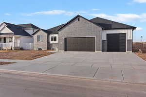 View of front of property featuring an attached garage, concrete driveway, and brick siding