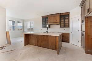 Kitchen with wood finish cabinetry, glass fronted cabinets, a center island with sink, and recessed lighting