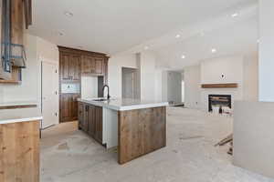 Kitchen with a center island with sink, a glass covered fireplace, vaulted ceiling, light stone countertops, and open floor plan