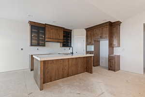 Kitchen featuring glass fronted cabinets, a kitchen island with sink, light countertops, wood finish cabinets, and recessed lighting