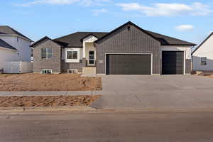 View of front of house featuring board and batten siding, an attached garage, concrete driveway, and brick siding