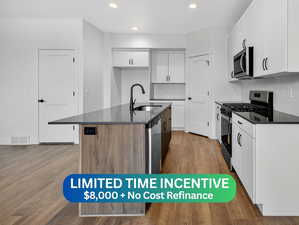 Kitchen with two tone cabinetry, stainless steel appliances, dark wood-type flooring, a center island with sink, and dark stone counters