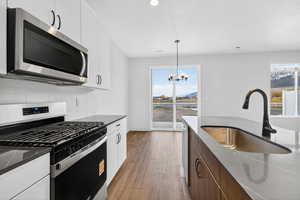 Two tone kitchen featuring stainless steel appliances, dark stone countertops, light wood-style flooring, dual tone cabinets, and tasteful backsplash