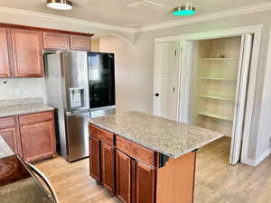 Kitchen featuring stainless steel refrigerator with ice dispenser, black range with electric cooktop, a kitchen island, light wood-type flooring, and ornamental molding