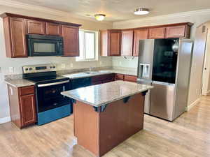Kitchen featuring black appliances, light stone countertops, light wood-style flooring, ornamental molding, and a center island