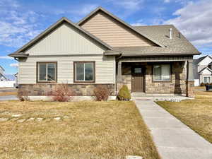 View of front facade with a front lawn, stone siding, covered porch, and a shingled roof